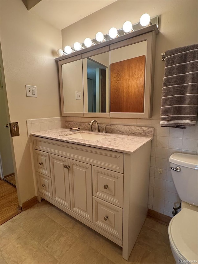 half bath with toilet, tile walls, and vanity