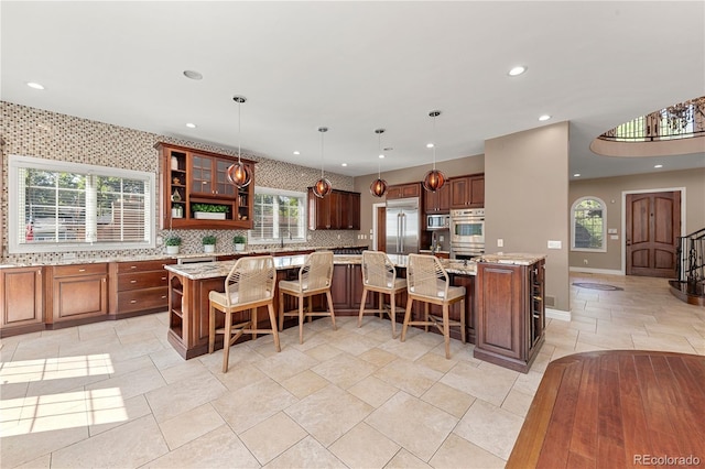 kitchen featuring a kitchen bar, hanging light fixtures, appliances with stainless steel finishes, light stone countertops, and a large island