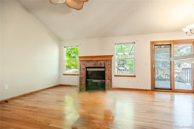 unfurnished living room with ceiling fan, light hardwood / wood-style floors, a fireplace, vaulted ceiling, and a textured ceiling