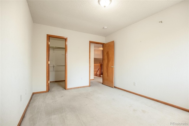 unfurnished bedroom featuring light carpet, a spacious closet, a closet, and a textured ceiling