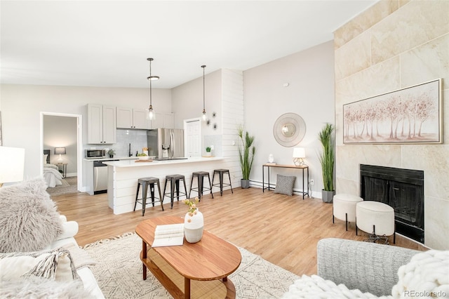 living room featuring lofted ceiling, a tile fireplace, a baseboard heating unit, and light hardwood / wood-style floors