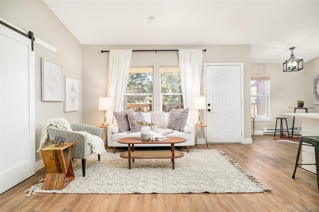 sitting room with an inviting chandelier, hardwood / wood-style floors, a baseboard heating unit, a wealth of natural light, and a barn door