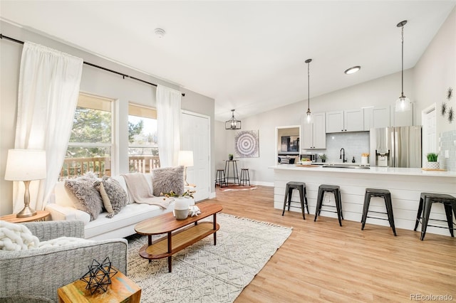 living room with sink, light hardwood / wood-style flooring, lofted ceiling, and a notable chandelier