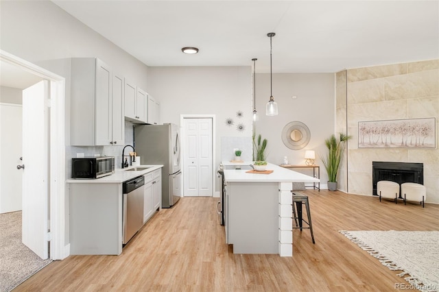 kitchen featuring hanging light fixtures, a breakfast bar area, a fireplace, appliances with stainless steel finishes, and sink