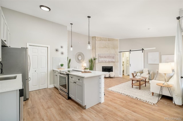 kitchen with stainless steel appliances, decorative light fixtures, light wood-type flooring, kitchen peninsula, and a barn door