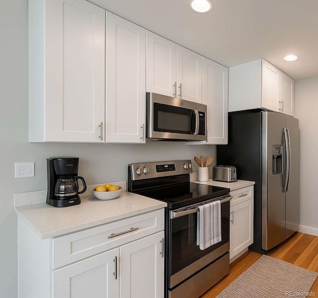 8239 Nola Dr, Denver, CO 80221 - kitchen with appliances with stainless steel finishes, light countertops, white cabinetry, light wood-style flooring, and recessed lighting