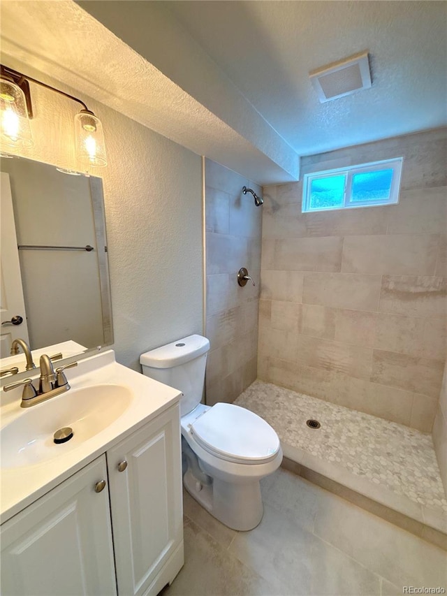 8239 Nola Dr, Denver, CO 80221 - bathroom featuring a textured wall, tiled shower, vanity, and a textured ceiling