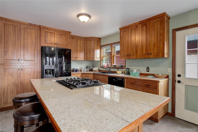 kitchen featuring a breakfast bar, brown cabinetry, a sink, and black appliances