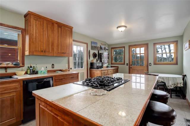 kitchen with a center island, brown cabinetry, black appliances, and a breakfast bar