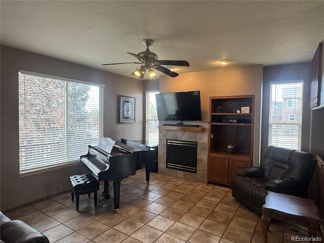 interior space featuring ceiling fan, light tile patterned floors, a tile fireplace, and a textured ceiling