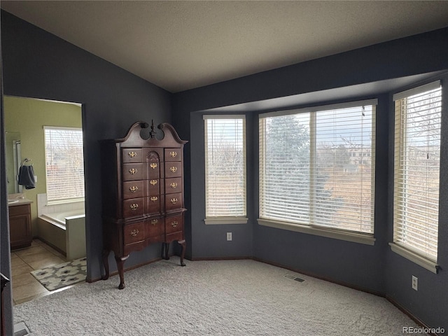 bedroom featuring ensuite bath, light carpet, and multiple windows