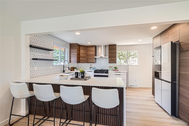 2065 Depew St, Edgewater, CO 80214 - kitchen with wall chimney exhaust hood, freestanding refrigerator, stainless steel range with gas stovetop, modern cabinets, and a kitchen bar