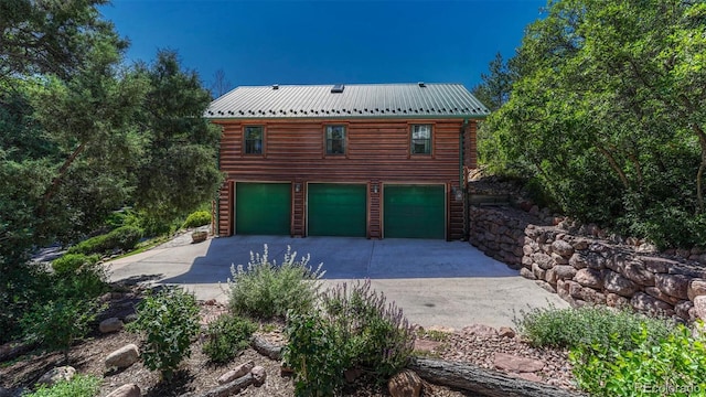 exterior space featuring log exterior, an attached garage, metal roof, and driveway