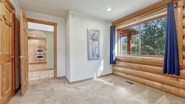 empty room featuring visible vents, baseboards, light colored carpet, arched walkways, and log walls