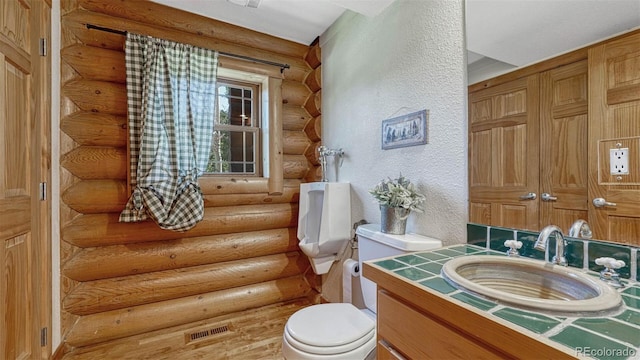 bathroom with vanity, toilet, a textured wall, and visible vents