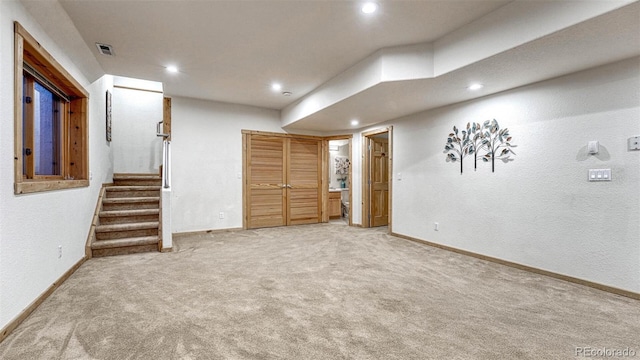 finished basement featuring stairway, baseboards, visible vents, and light carpet