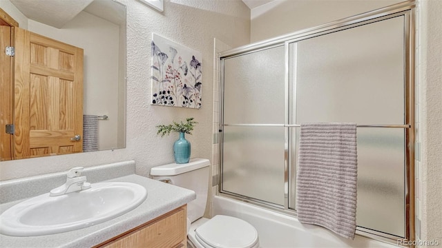 bathroom featuring vanity, toilet, bath / shower combo with glass door, and a textured wall