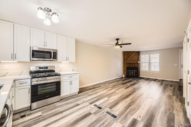 kitchen featuring white cabinets, ceiling fan, a fireplace, and stainless steel appliances