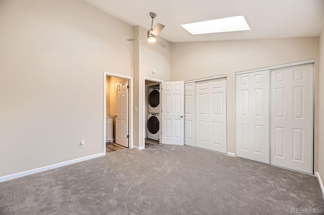 unfurnished bedroom with carpet, two closets, stacked washer and dryer, a skylight, and ceiling fan