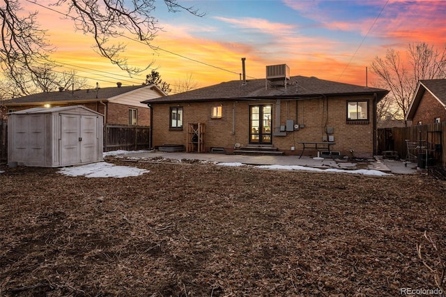 back house at dusk featuring a shed, central AC unit, and a patio area