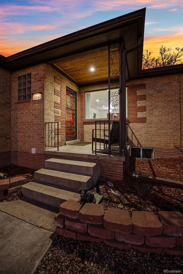 exterior entry at dusk featuring covered porch and brick siding