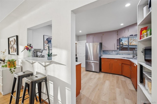 kitchen featuring open shelves, freestanding refrigerator, light countertops, a sink, and light wood finished floors