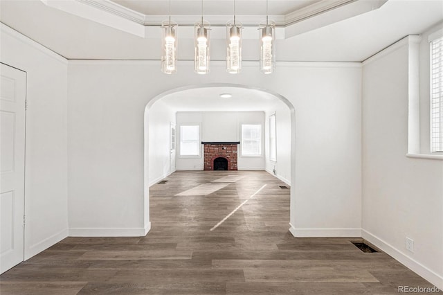 unfurnished dining area with a tray ceiling, dark hardwood / wood-style flooring, crown molding, and a fireplace