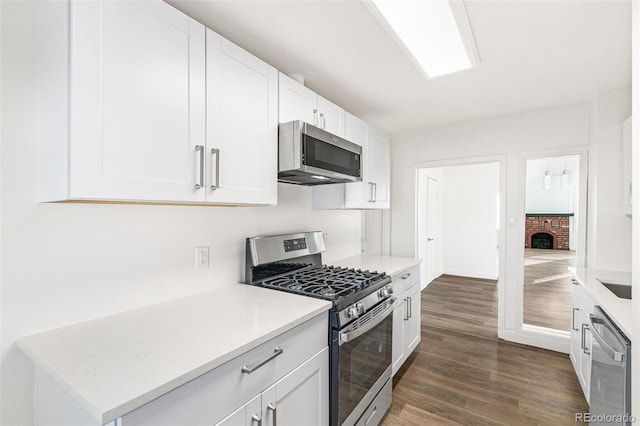 kitchen featuring white cabinetry, stainless steel appliances, dark hardwood / wood-style floors, and a brick fireplace