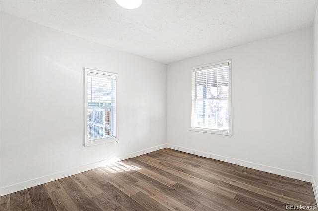 empty room with a textured ceiling, a wealth of natural light, and dark wood-type flooring