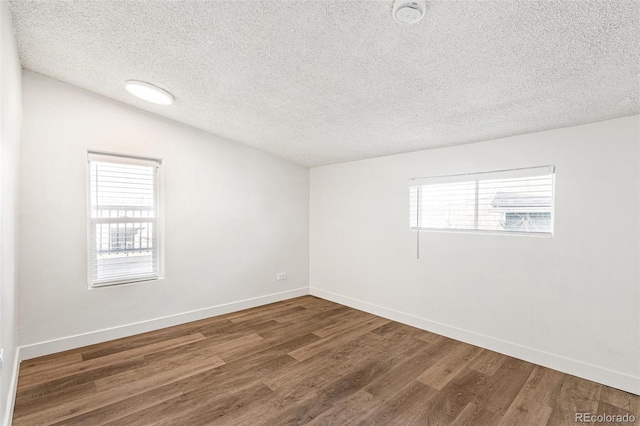 unfurnished room featuring dark hardwood / wood-style floors, a textured ceiling, a wealth of natural light, and vaulted ceiling