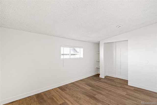 unfurnished bedroom with vaulted ceiling, a closet, hardwood / wood-style floors, and a textured ceiling