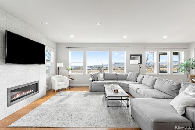 living area with baseboards, recessed lighting, a fireplace, and light wood-style floors