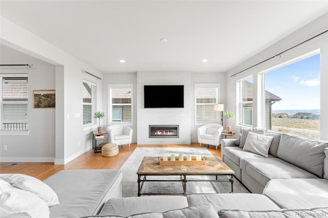 living area with recessed lighting, a large fireplace, light wood-style flooring, and baseboards