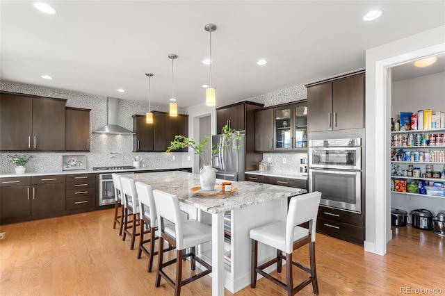 kitchen featuring a breakfast bar, a kitchen island, wall chimney range hood, and dark brown cabinets