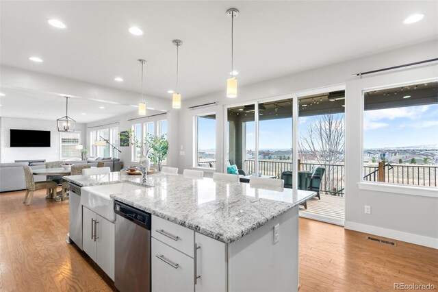 kitchen featuring an island with sink, white cabinetry, open floor plan, and stainless steel dishwasher