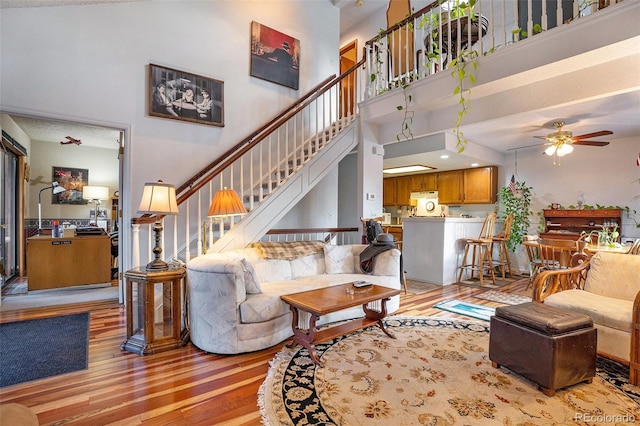 living area featuring a towering ceiling, light wood-type flooring, and a ceiling fan