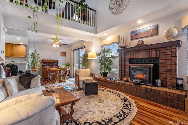 living room featuring wood finished floors, a ceiling fan, a high ceiling, a fireplace, and recessed lighting