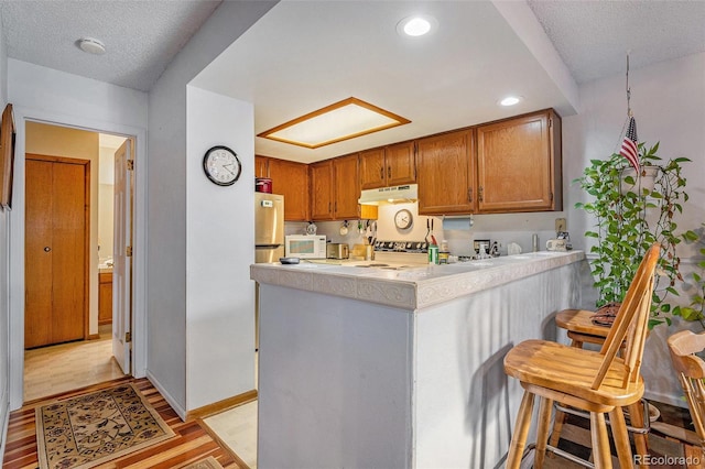 kitchen featuring under cabinet range hood, a breakfast bar, light wood finished floors, a peninsula, and light countertops