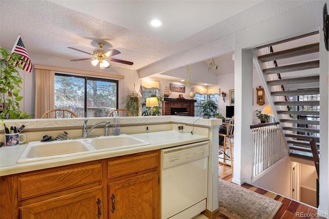 kitchen with a sink, a textured ceiling, a fireplace, a ceiling fan, and white dishwasher