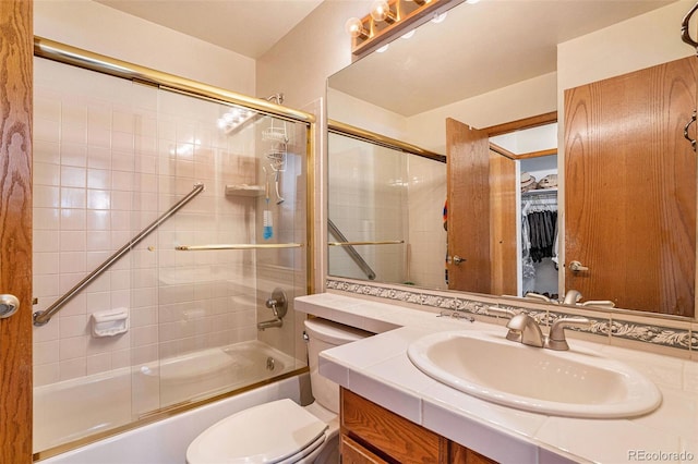 bathroom featuring a walk in closet, toilet, bath / shower combo with glass door, and vanity