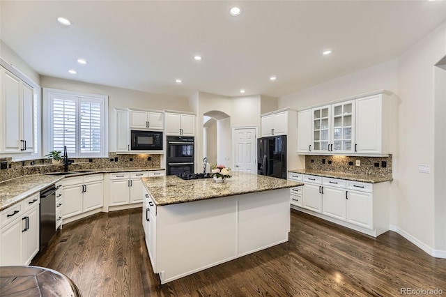 kitchen featuring black appliances, a center island, light stone countertops, tasteful backsplash, and white cabinetry