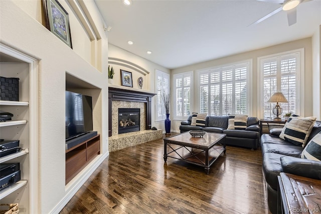 living room featuring ceiling fan, built in features, dark wood-type flooring, and a high end fireplace