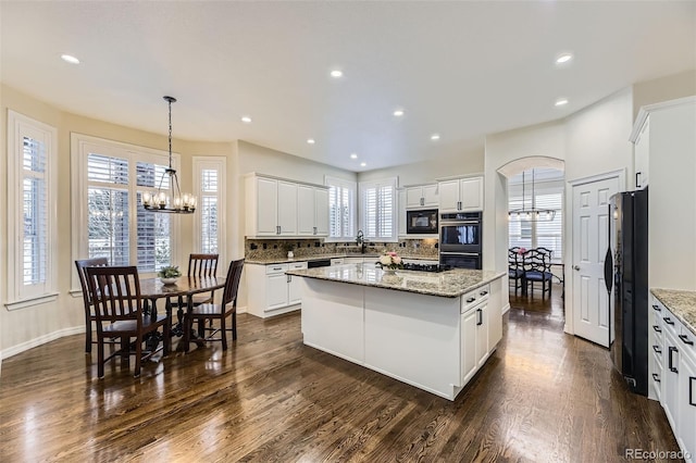 kitchen with white cabinets, black appliances, a kitchen island, an inviting chandelier, and decorative backsplash