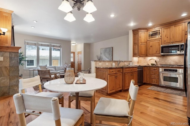 kitchen with tasteful backsplash, decorative light fixtures, stone counters, light wood-type flooring, and appliances with stainless steel finishes