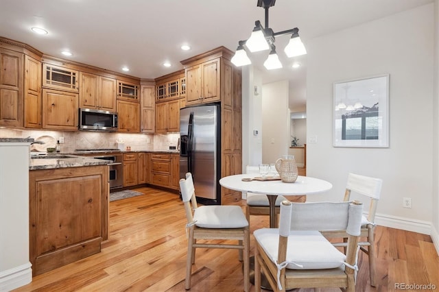 kitchen featuring stainless steel appliances, tasteful backsplash, hanging light fixtures, light stone countertops, and light hardwood / wood-style flooring