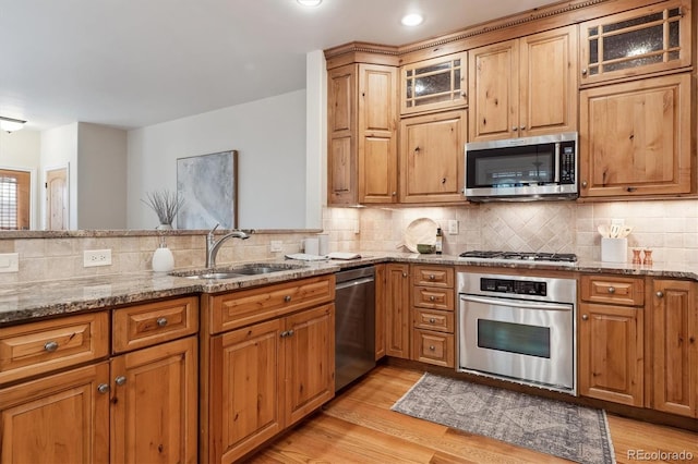 kitchen featuring stainless steel appliances, light hardwood / wood-style floors, sink, backsplash, and light stone counters