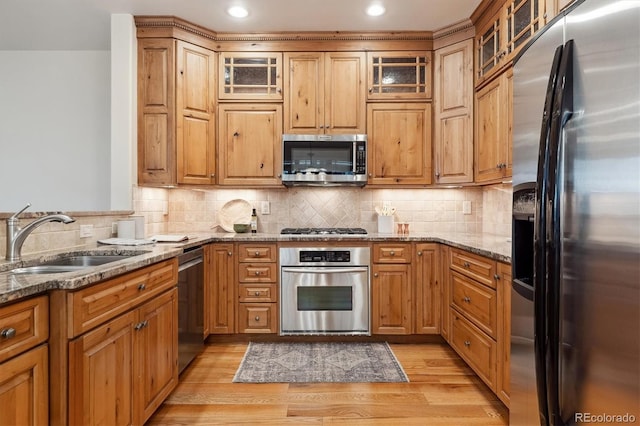 kitchen featuring appliances with stainless steel finishes, decorative backsplash, sink, light hardwood / wood-style floors, and light stone counters