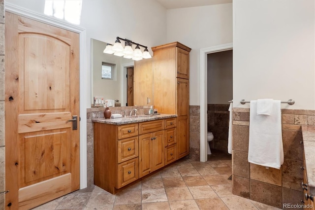 bathroom featuring toilet, vanity, and tile walls