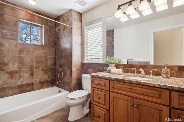 full bathroom with toilet, tiled shower / bath combo, tile patterned flooring, tile walls, and vanity