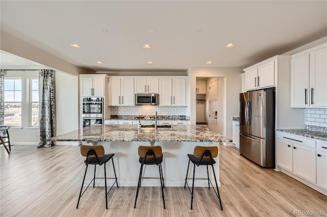 kitchen featuring light stone counters, appliances with stainless steel finishes, and a kitchen island with sink